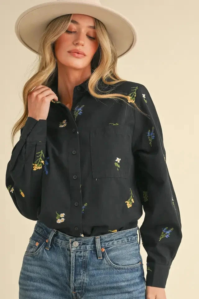 Woman wearing a black embroidered shirt and jeans with a beige background