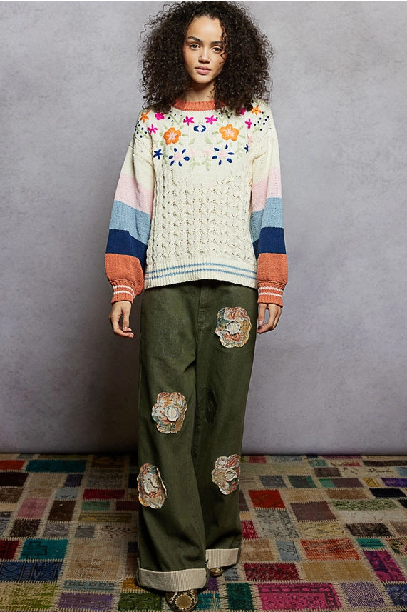 Woman wearing a colorful sweater and green pants with floral patches on a patterned rug.