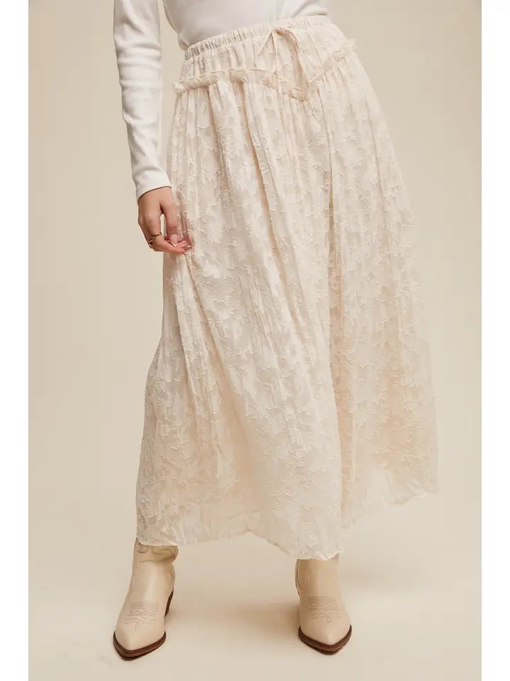 Person wearing a long beige skirt with a plain background