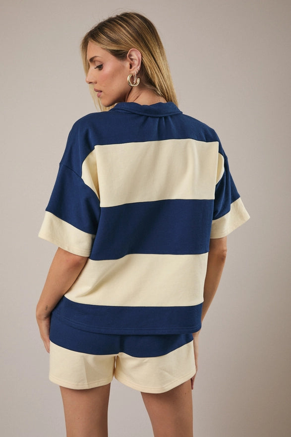 Model is wearing a matching cream and navy striped set with shorts and a half zip polo like top.