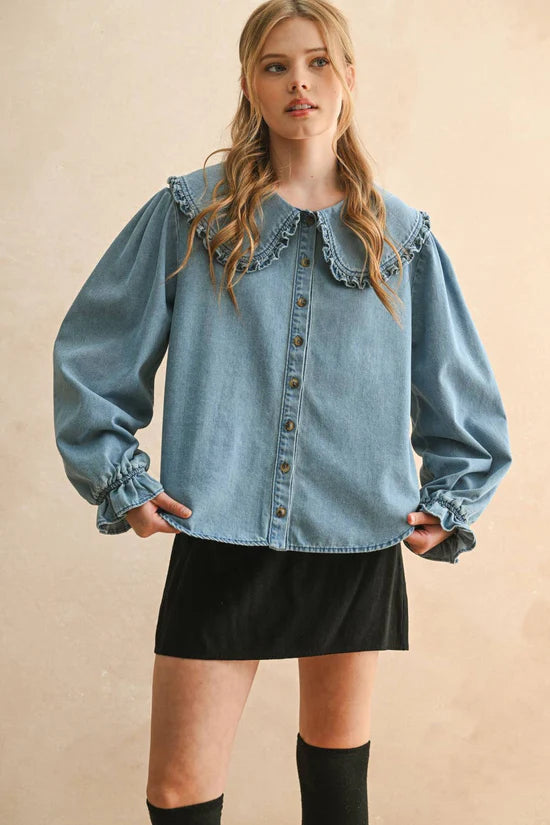 Woman wearing a denim blouse with ruffled collar and long sleeves on a beige background