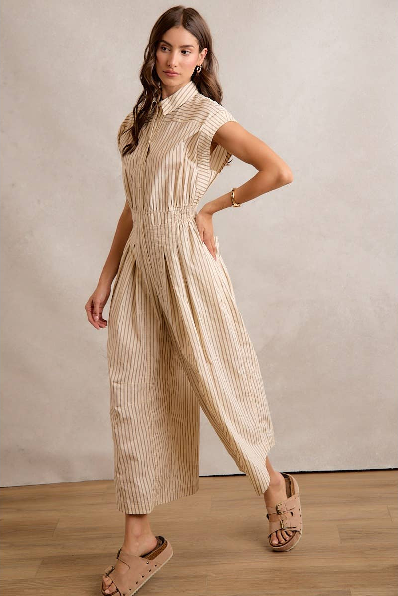 Woman wearing a beige and white striped jumpsuit against a plain background