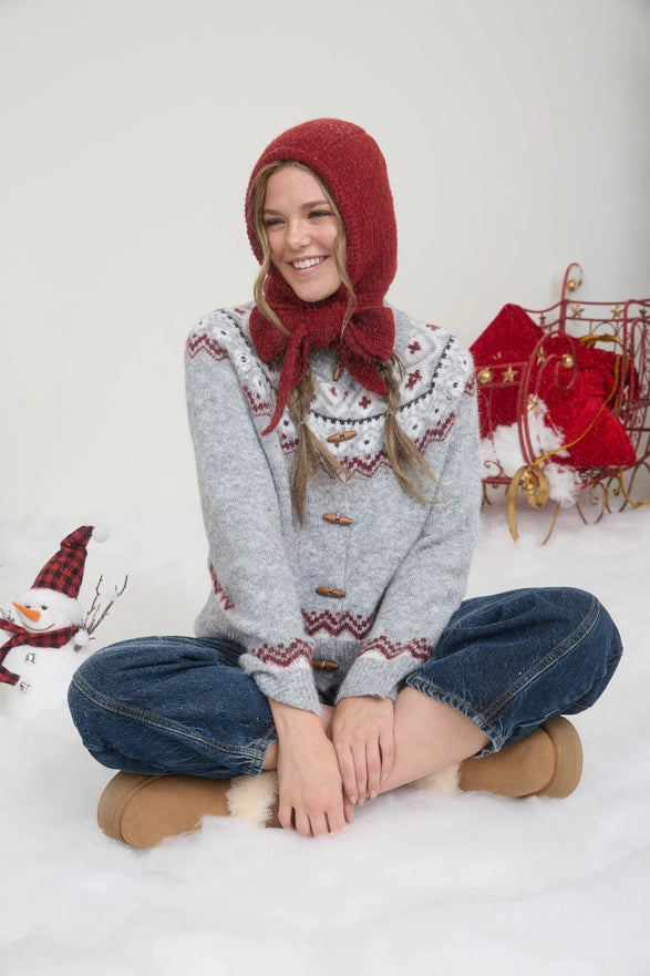 Person wearing a patterned sweater and red bonnet sitting on the ground with Christmas decorations in the background.