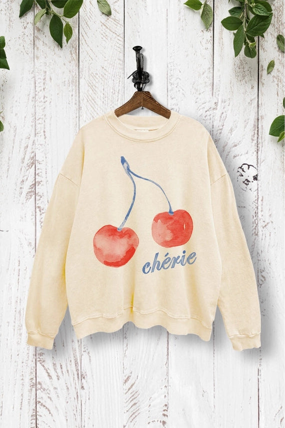 Beige sweatshirt with cherry design and 'chérie' text on a wooden background