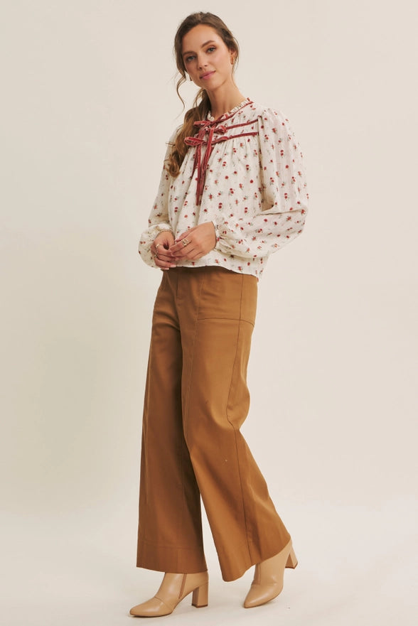 Woman wearing a patterned blouse and wide-leg pants on a plain background