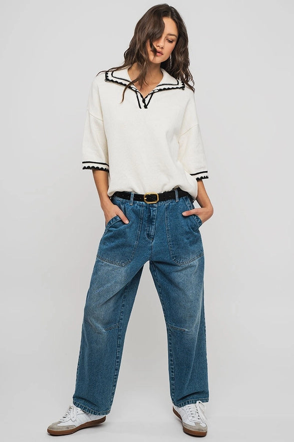 Woman wearing a white blouse with black trim and blue jeans on a plain background