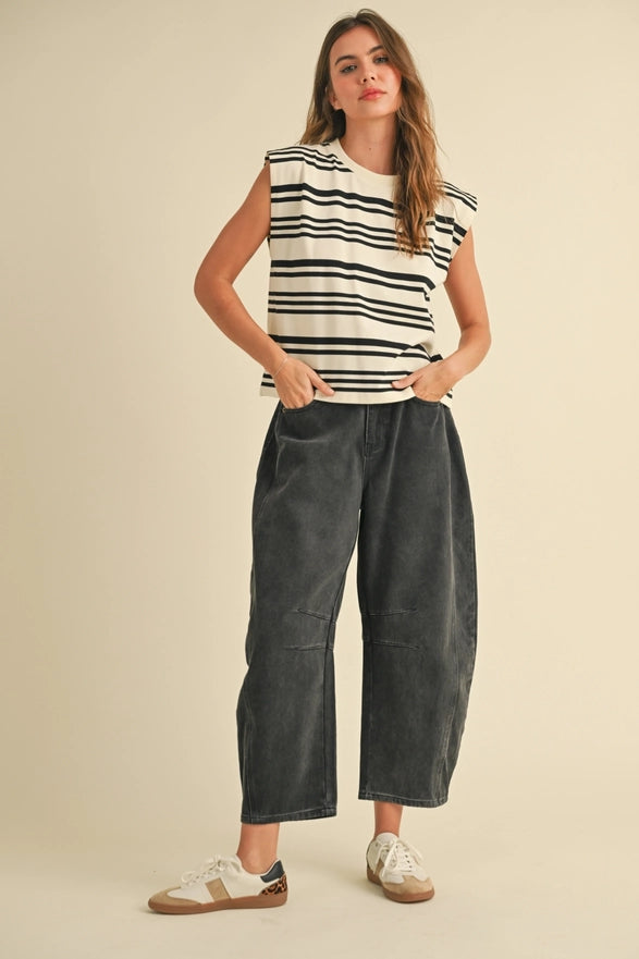 Woman wearing a striped sleeveless top and dark jeans on a beige background