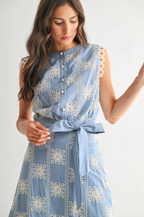 Woman wearing a blue dress with white floral embroidery on a plain background
