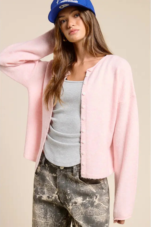 Woman wearing a pink cardigan, gray tank top, and distressed jeans with a blue cap.