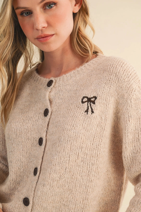 Woman wearing a beige cardigan with black buttons and a bow design.