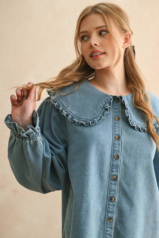 Woman wearing a blue denim shirt with ruffled collar against a beige background
