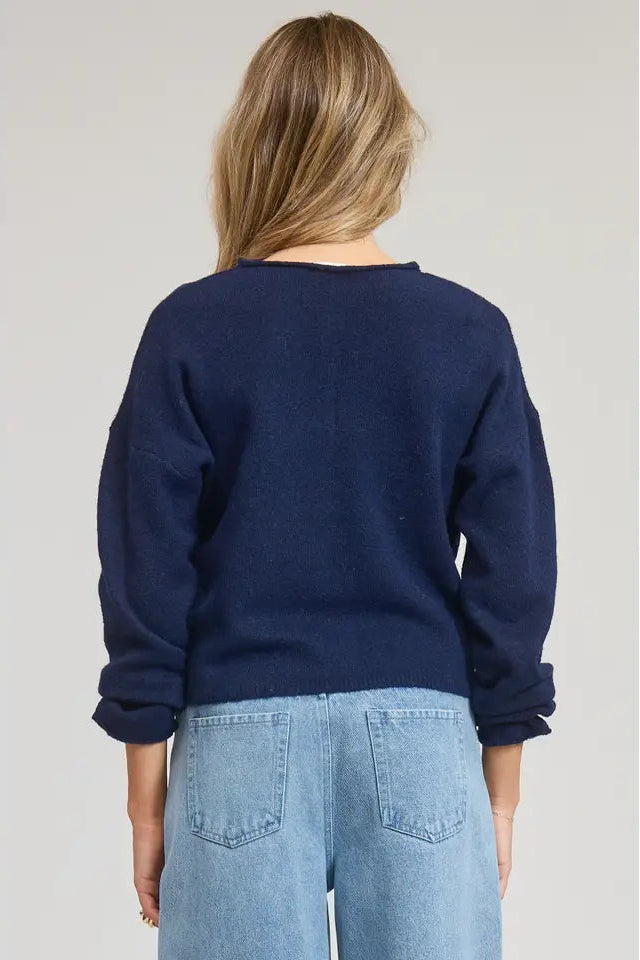 Person wearing a navy blue sweater and light blue jeans on a plain background