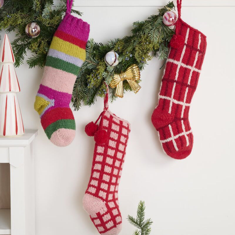 Colorful Christmas stockings hanging on a fireplace with decorative trees and ornaments.