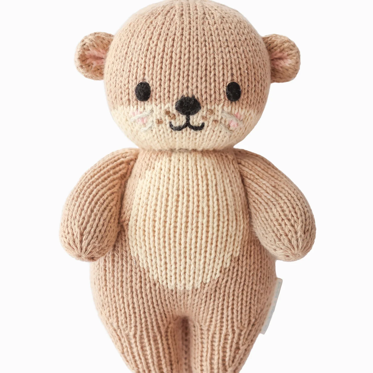 A knitted teddy bear plush toy in a soft light beige color, featuring black embroidered eyes, nose, and mouth, set against a plain white background.