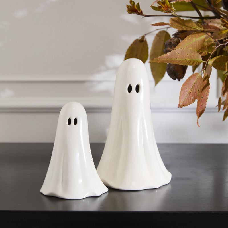 Two white ghost-shaped salt and pepper shakers on a dark surface with a blurred background.