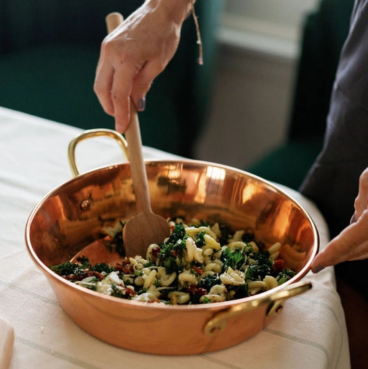 Person stirring food in a copper pan on a table