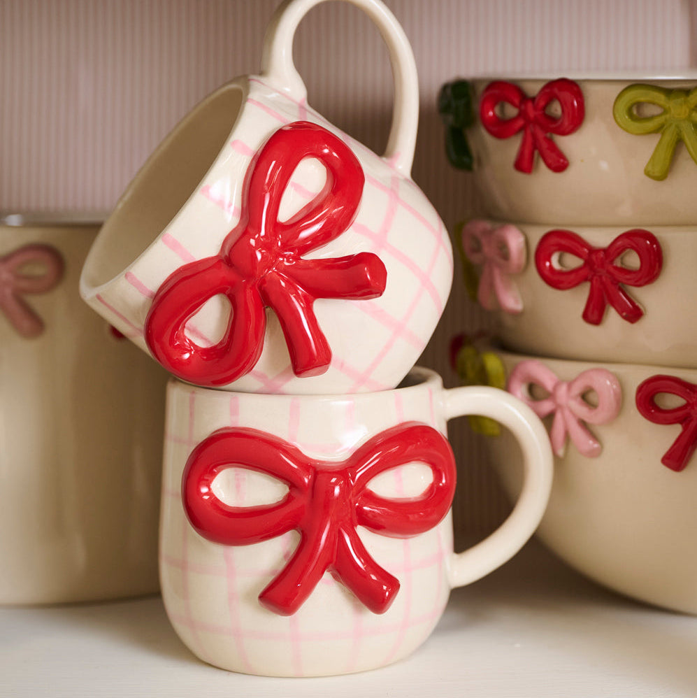 Set of ceramic mugs with red bow designs on a white surface